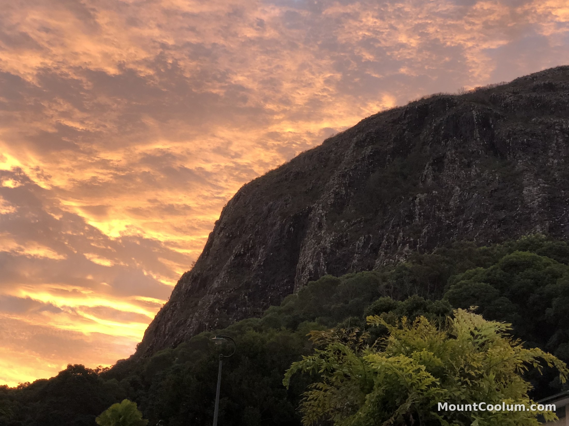 Mount Coolum's volcanic dome silhouetted against a glowing sunset sky, seen from the base of the mountain